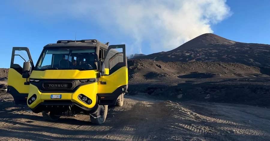 Un fuoristrada giallo parcheggiato sul ghiaino vulcanico a Etna Nord, con la cima che fuma alle spalle