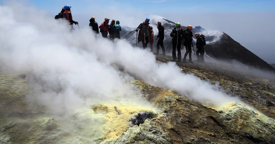 Escursionisti con il casco sul bordo di un cratere sommitale fumante dell'Etna, zolfo giallo sulle rocce