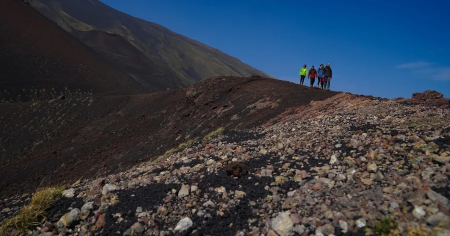 Escursionisti su una cresta craterica color ruggine in alto sull'Etna, sotto un cielo blu intenso
