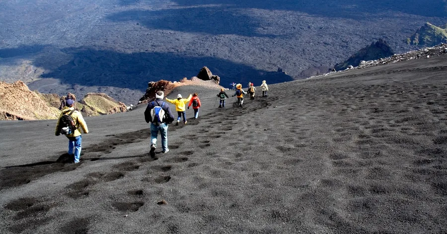 Una fila di escursionisti che sale sulla sabbia vulcanica nera verso il cono sommitale dell'Etna