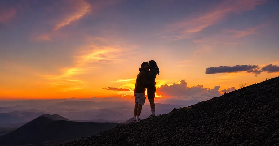 Due escursionisti in controluce su un pendio dell'Etna contro il cielo arancione del tramonto